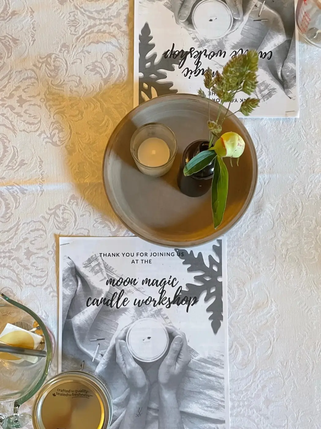 A candle-making workshop table set with herbs, a candle and a welcome card
