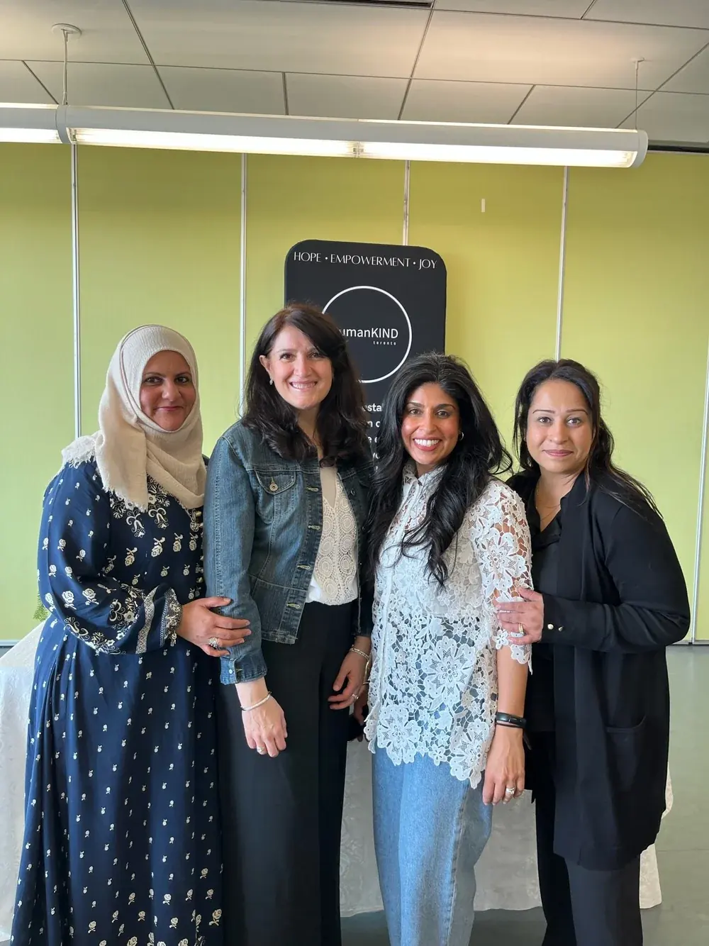 Four women smiling in front of the humanKIND banner at a Create for a Cause event