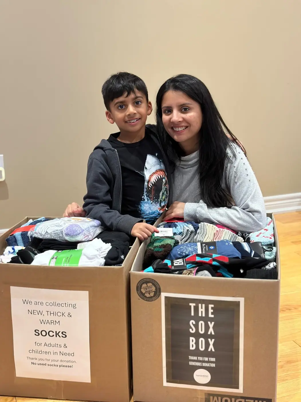 A young donor and a volunteer with two Sox Boxes overflowing with new socks