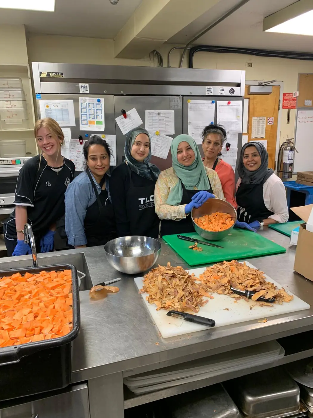 A group of volunteers smiling in a commercial kitchen while preparing food